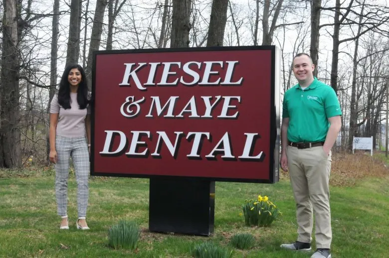 Two people standing beside Kiesel & Maye Dental sign